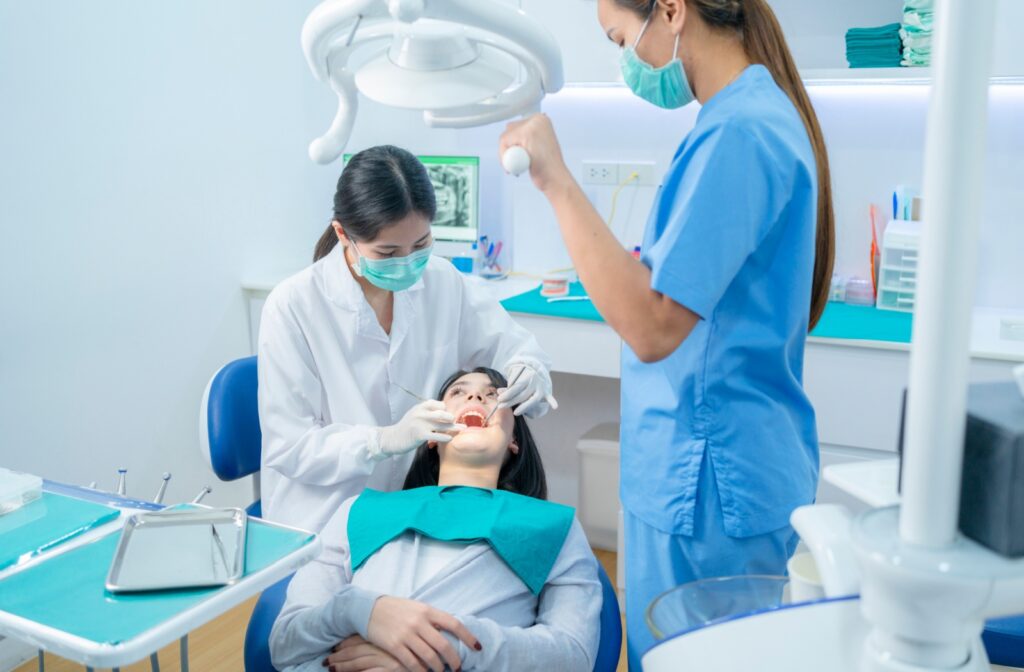 A female patient undergoing a procedure to fill her cavity as a dentist and dental hygenist hold dental equipment.