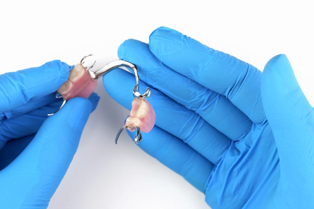 A close-up image of a dentist wearing blue gloves and showing off a set of partial dentures.