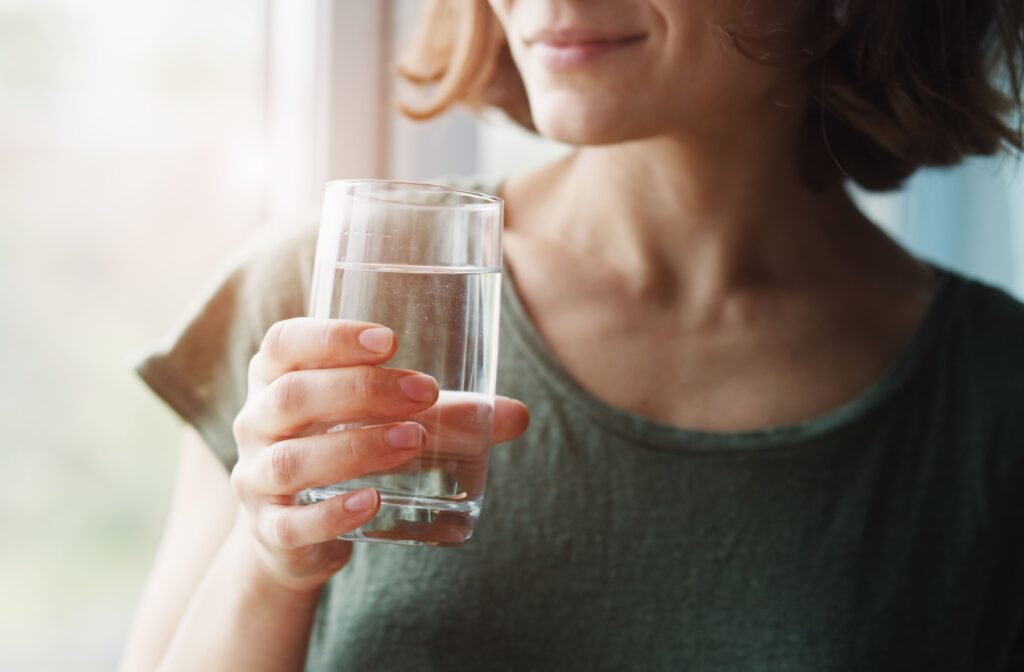 An adult stays hydrated by sipping on water to help their body heal from a recent tooth extraction.