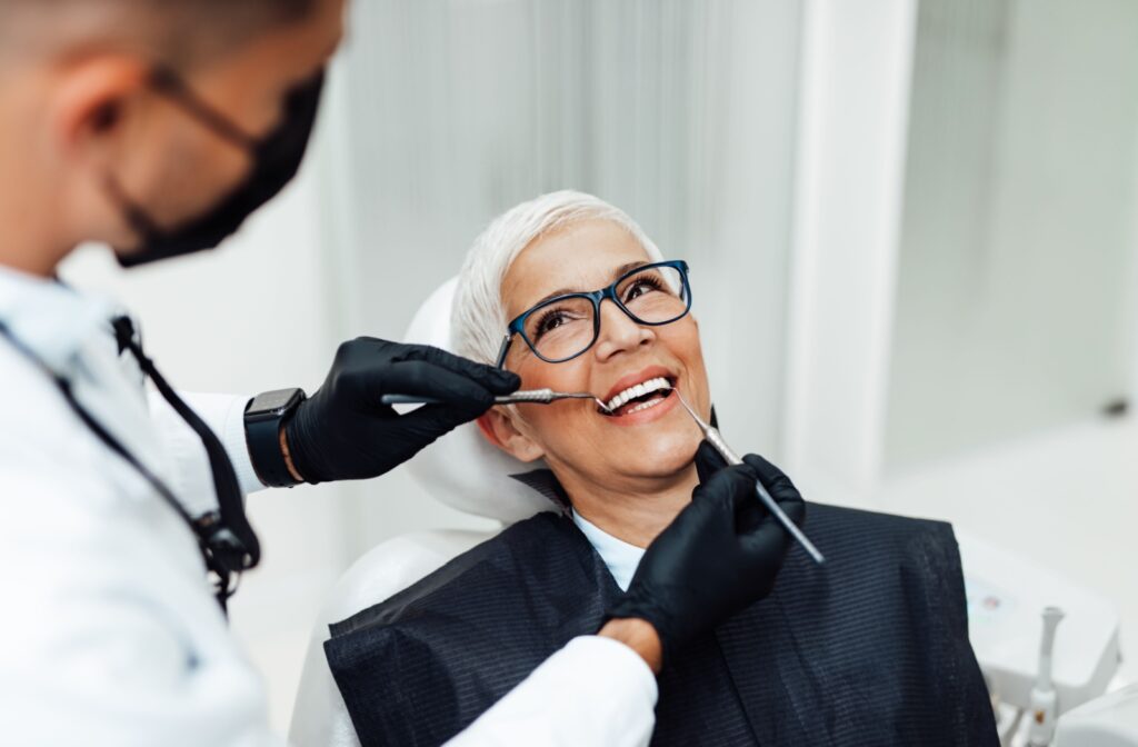 A patient in a dental chair smiling while a dentist uses tools to examine teeth during a dental recall exam.