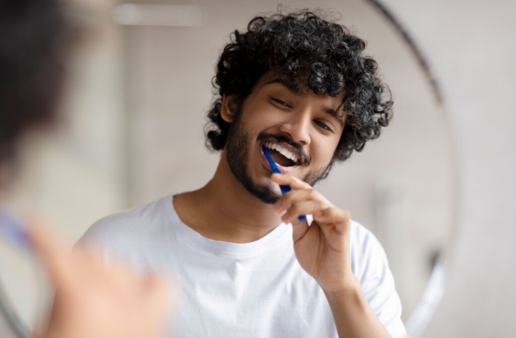 A man brushing his teeth while looking in the mirror.