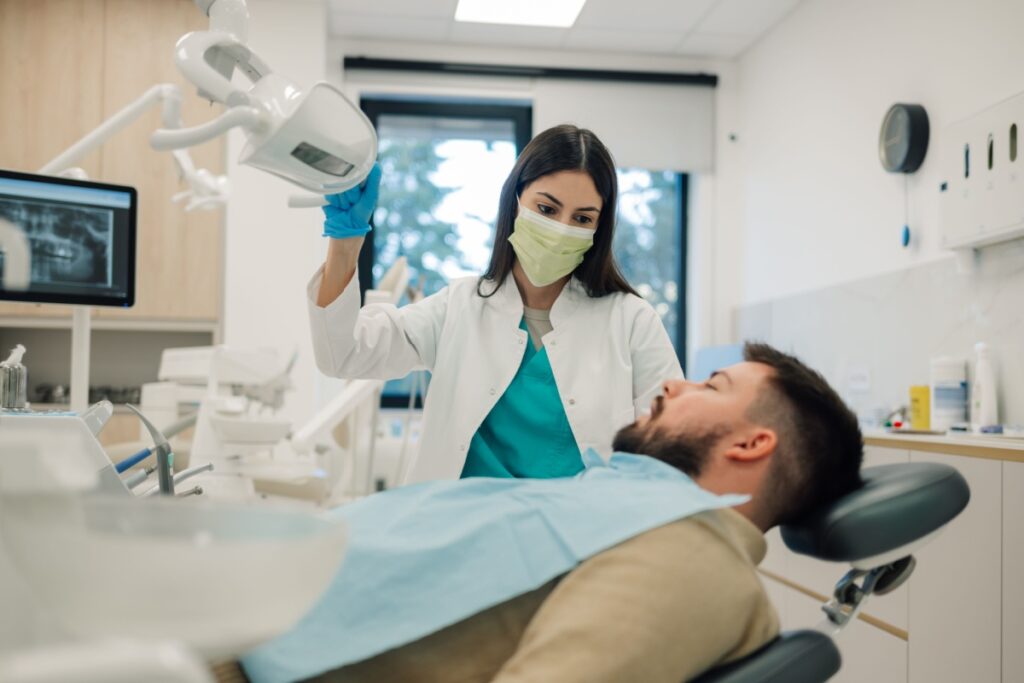 Dentist adjusting overhead light as patient lays on chair.