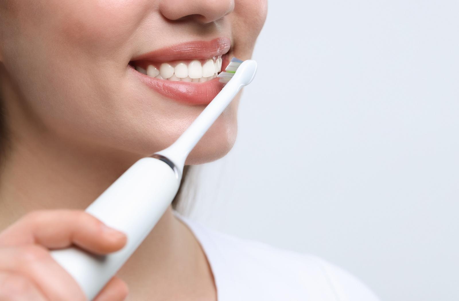 Smiling woman brushing her teeth with an electric toothbrush.